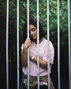 woman wearing pink crew neck t shirt standing and leaning behind white bars