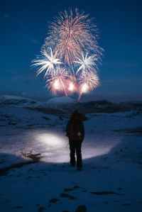 person stands on snow covered mountain looking at fireworks